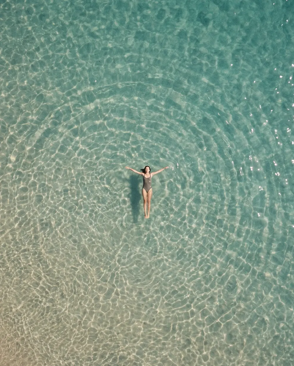 A woman floating on her back in clear turquoise water, seen from above