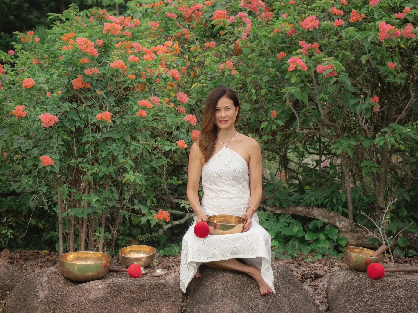 Claire seated with singing bowls beneath a flowering bush
